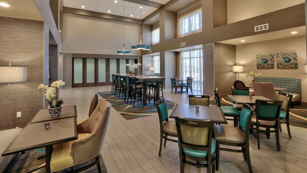 A spacious hotel lobby with multiple dining areas, comfortable seating, and large windows allowing natural light. - Hampton Inn & Suites Albuquerque Airport (Albuquerque)