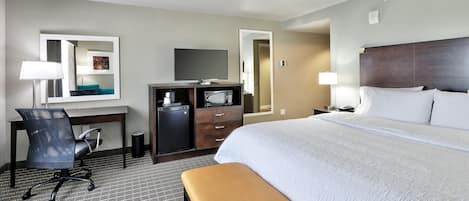 A hotel room with a bed, desk, chair, television, and a small refrigerator.