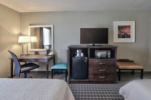 Une chambre d’hôtel comprenant un lit, un bureau avec une chaise, une télévision, un minibar et une petite table avec une chaise.