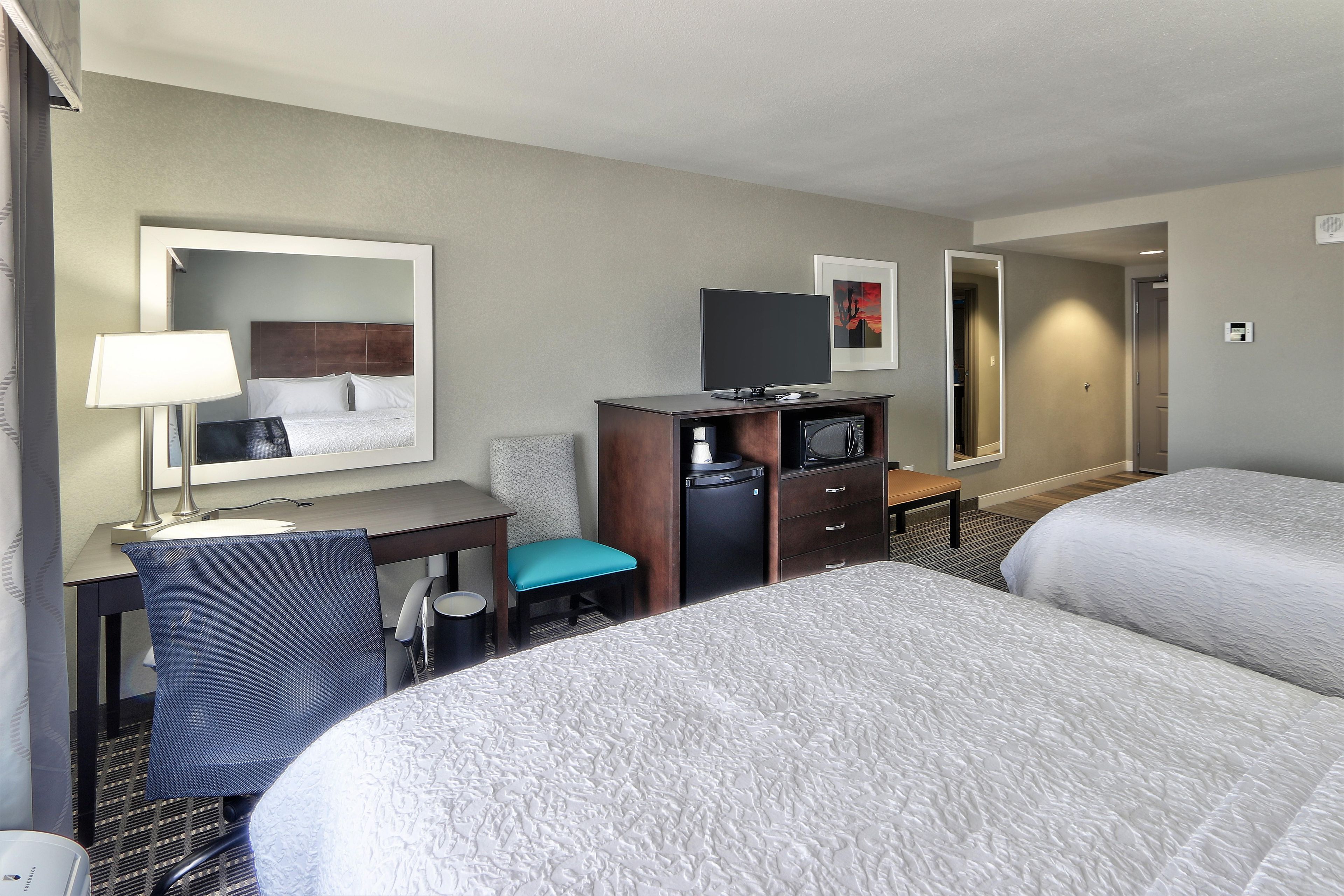 A hotel room with two beds, a desk with a chair, a television, and a small refrigerator.