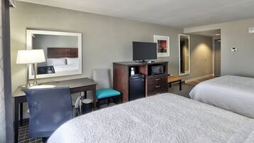 A hotel room with two beds, a desk with a chair, a television, and a small refrigerator.