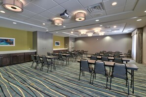 Une salle de conférence équipée de tables et de chaises, d’un projecteur et d’un sol recouvert de moquette.