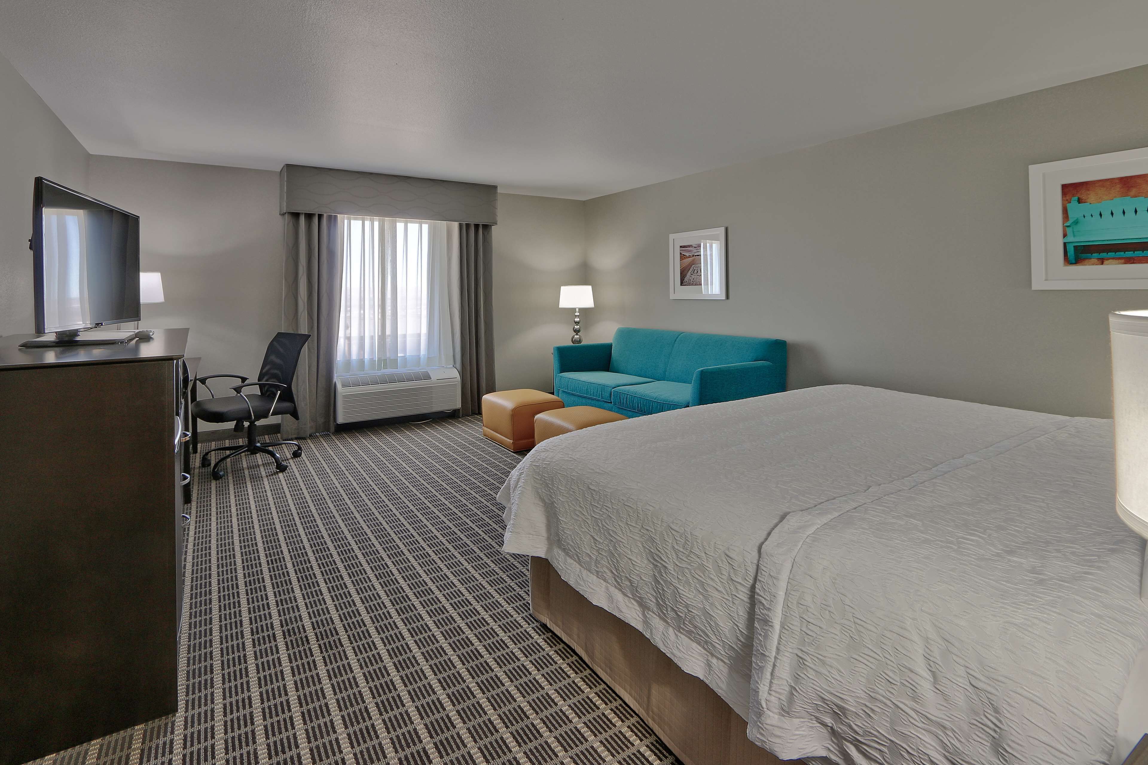 Habitación de hotel con una cama grande, un escritorio con computadora, una silla, un sofá y un televisor.