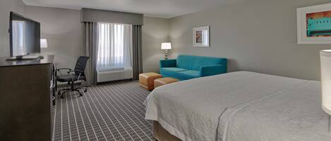 Habitación de hotel con una cama grande, un escritorio con computadora, una silla, un sofá y un televisor.