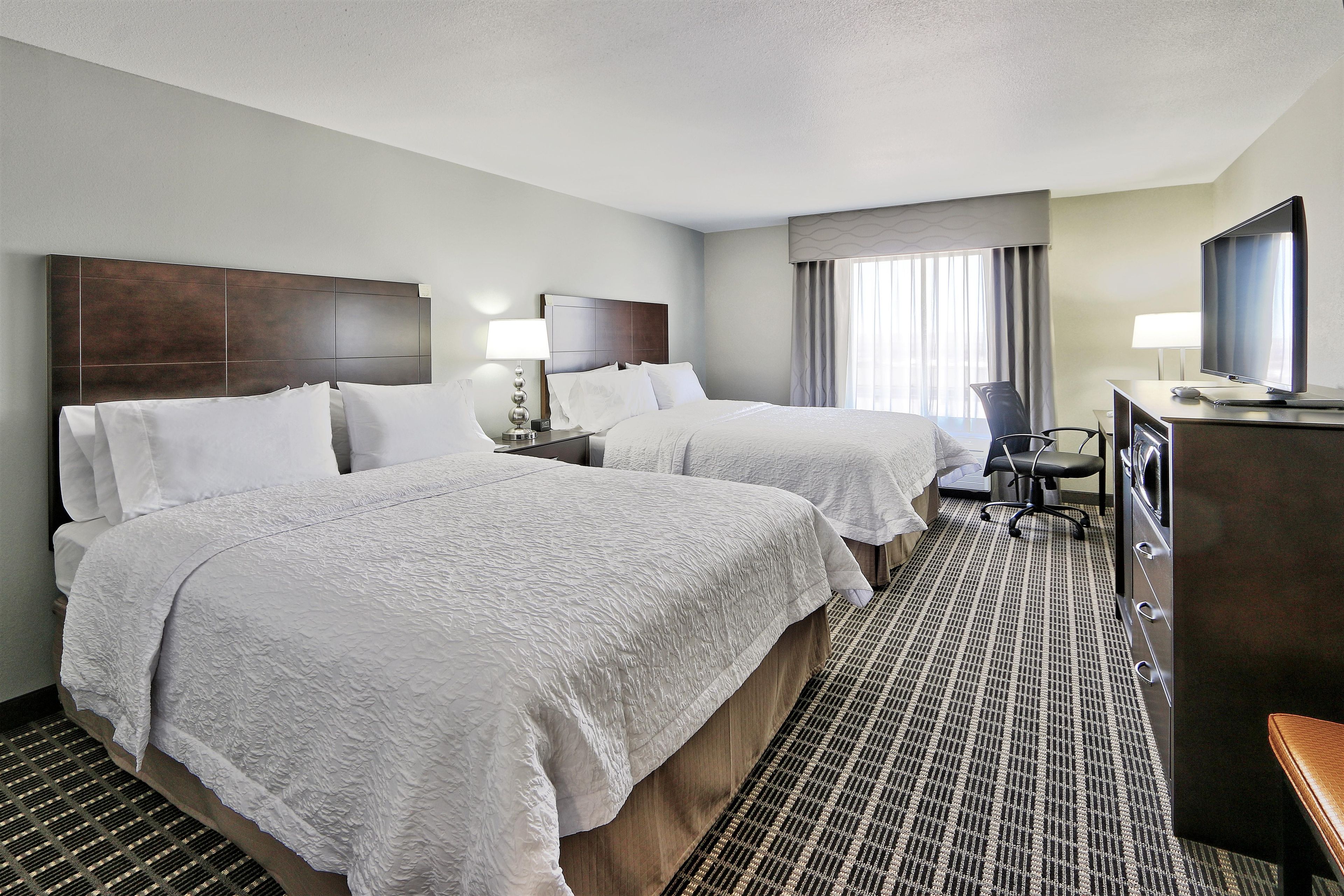 A hotel room with two beds, a desk, a chair, and a television.