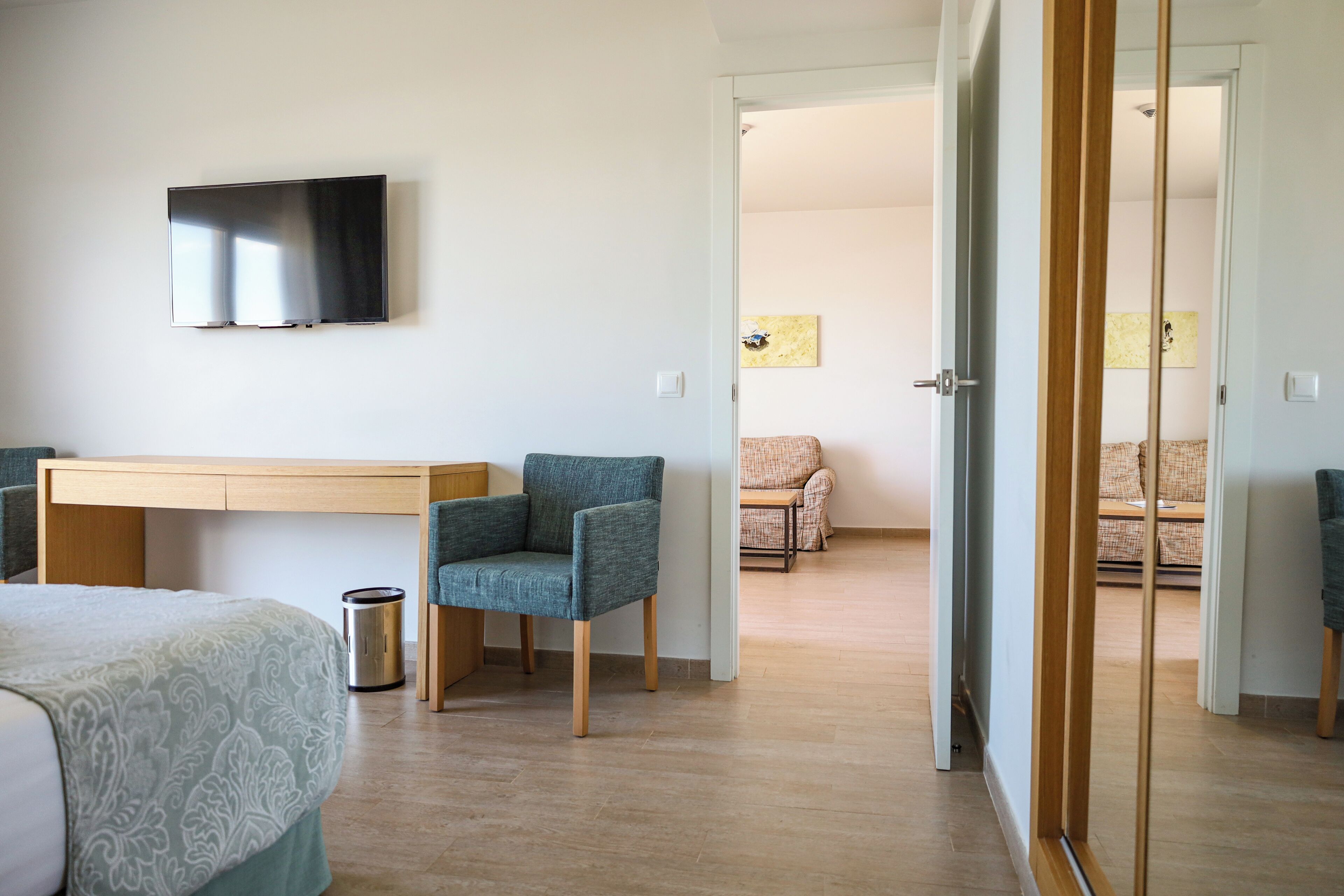 Una camera d'albergo con un letto, una scrivania, una sedia, una televisione e una porta che dà su un'altra stanza.