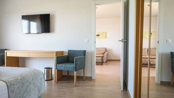 Una camera d'albergo con un letto, una scrivania, una sedia, una televisione e una porta che dà su un'altra stanza.