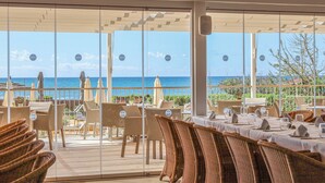 Un restaurante con vistas al mar, con sillas y mesas de mimbre preparadas para comer.