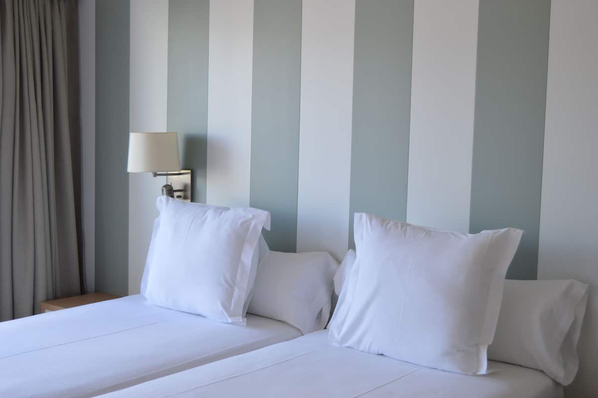 A hotel room with a bed, white pillows, a nightstand, a lamp, and a striped wall.