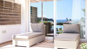Un espacio de estar moderno al aire libre con dos sofás y una mesita, con vista a una piscina y una playa.