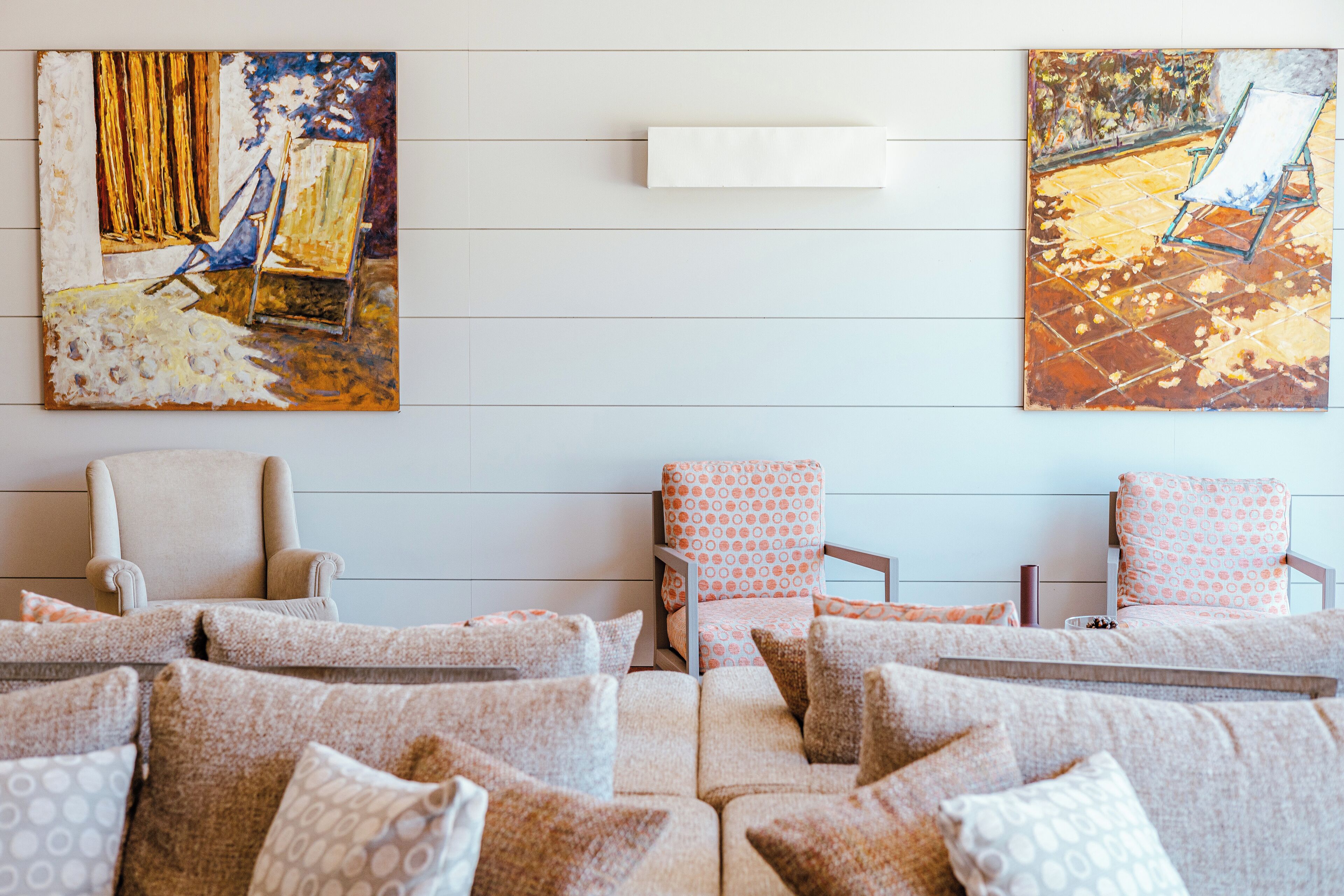 A living room with a sofa set, two armchairs, and two paintings on the wall.