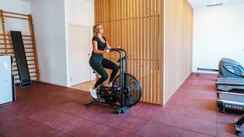 Una mujer usando una máquina elíptica en una habitación con un revestimiento de listones de madera, una cinta de correr y una puerta.