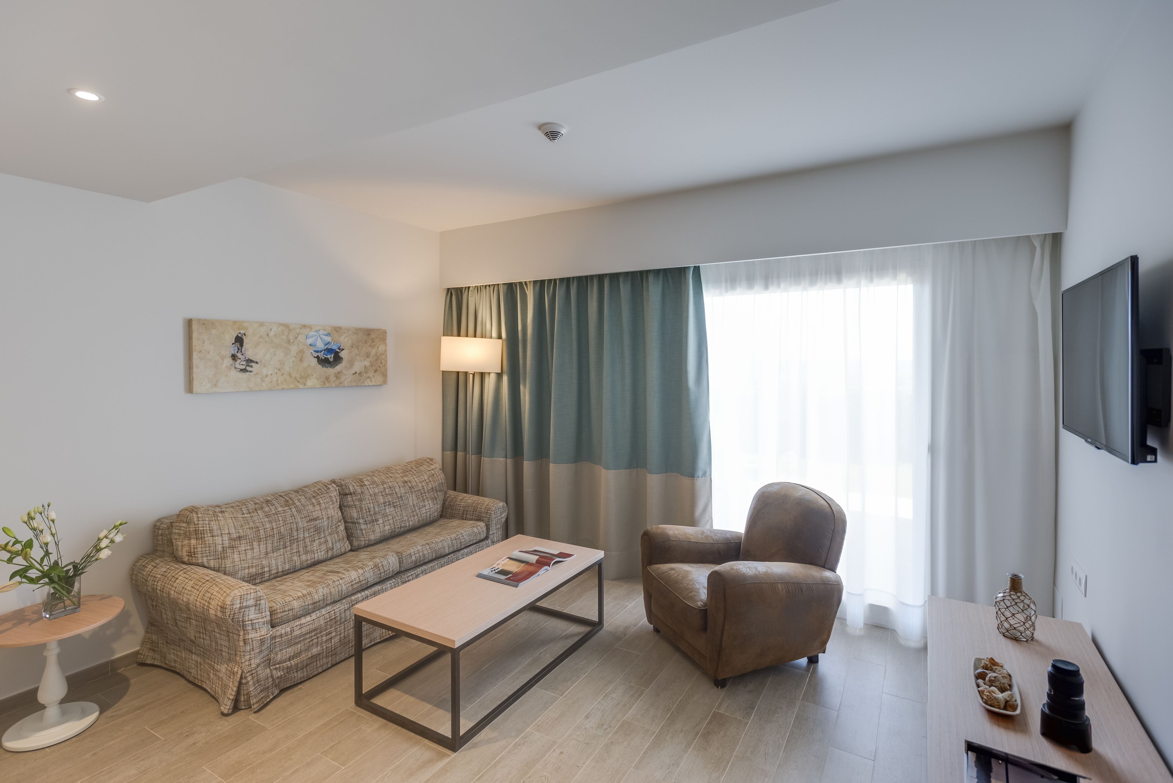A modern living room with a sofa, armchair, coffee table, and a flat-screen TV.