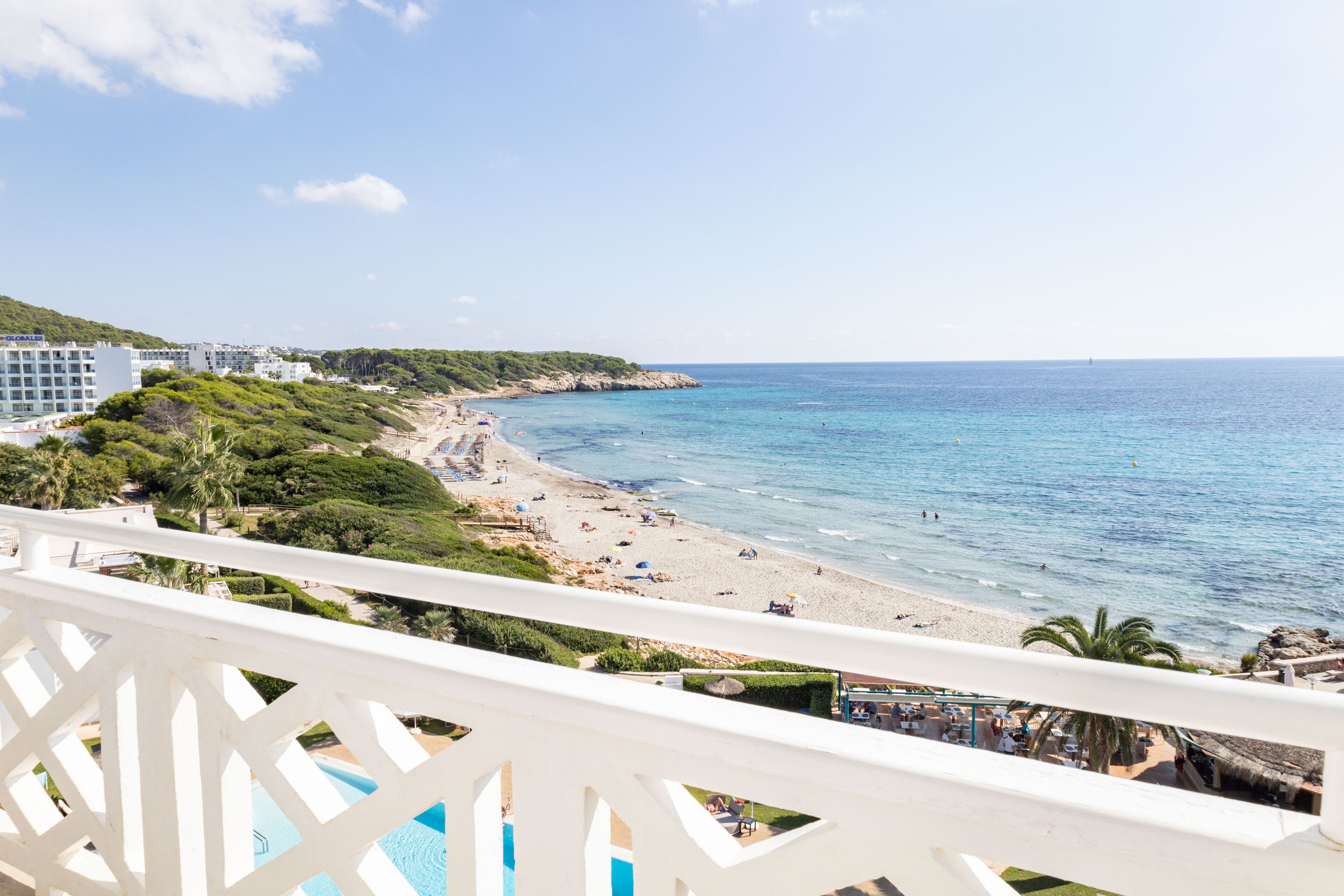 A beach view from a balcony with a pool, beach umbrellas, and a clear sky.