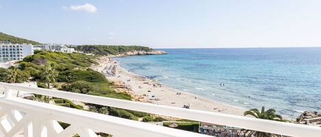 A beach view from a balcony with a pool, beach umbrellas, and a clear sky.