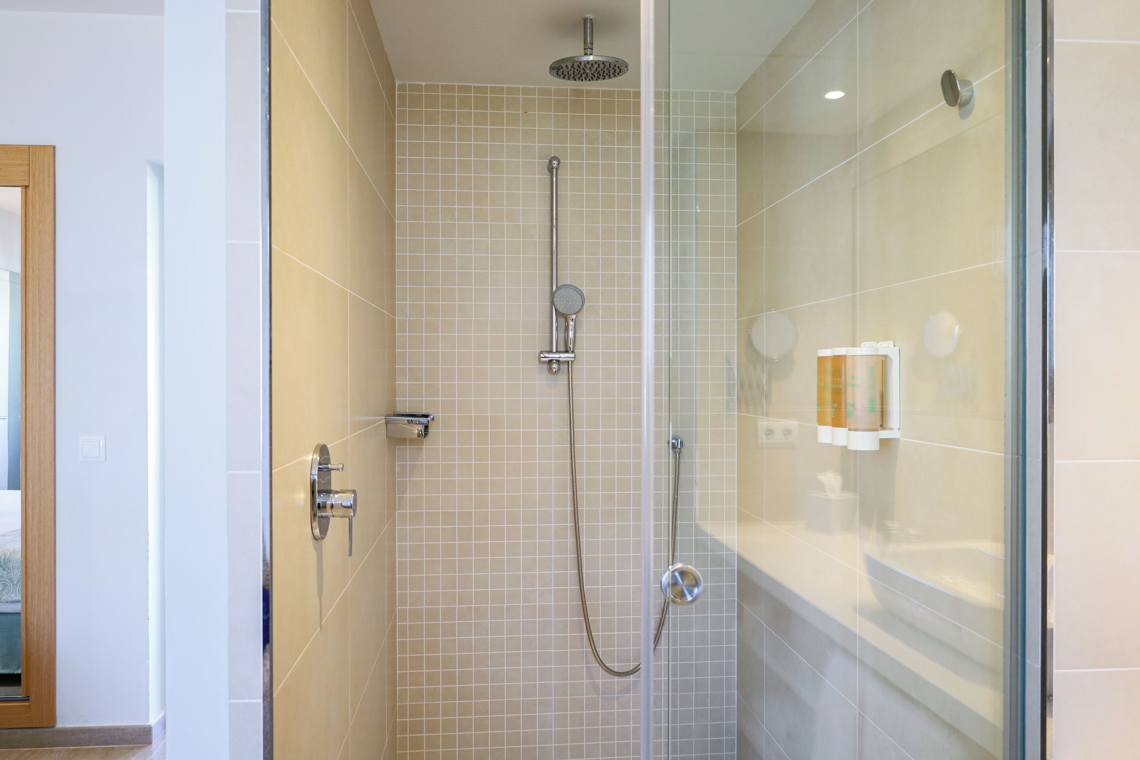 Un baño moderno con cabina de ducha de vidrio, paredes con azulejos y un dispensador de papel higiénico visible.