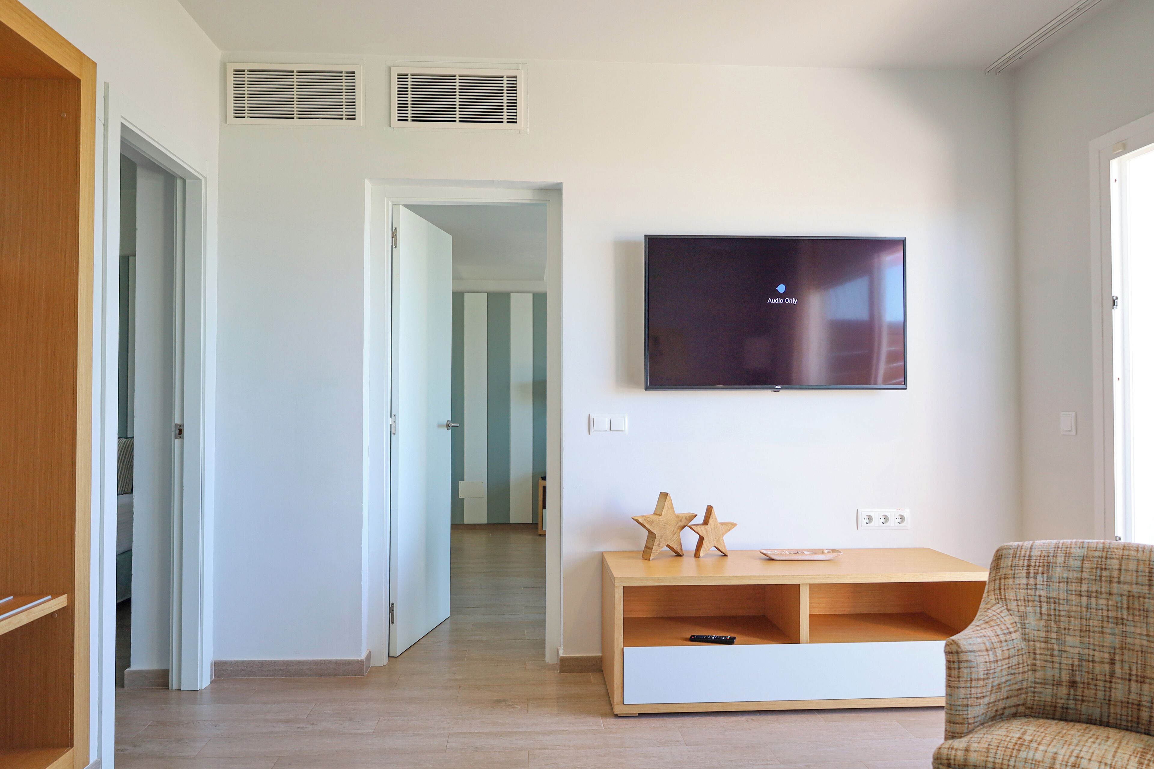 Una sala de estar moderna con un televisor de pantalla plana montado en la pared, un mueble de entretenimiento de madera y un sillón a cuadros.