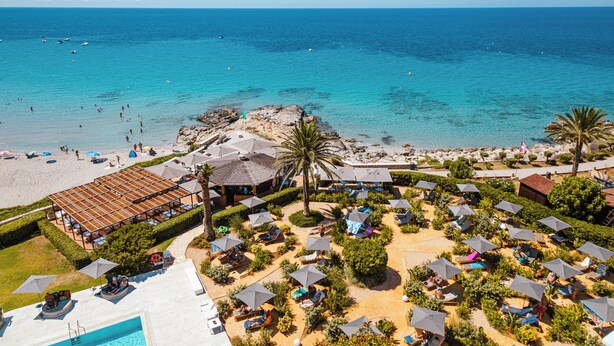 Vista aérea de un complejo turístico en la playa con numerosas tumbonas, sombrillas y una zona de piscina.