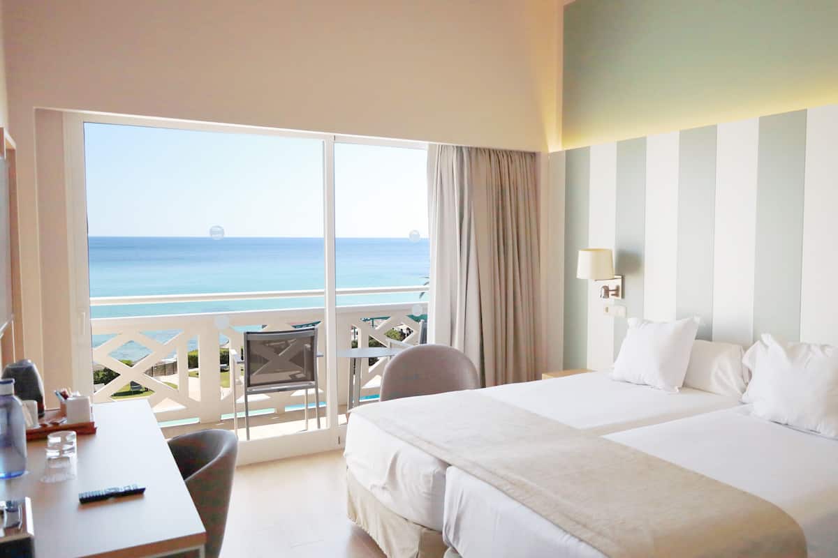 A hotel room with a bed, a desk, a chair, and a view of the ocean.