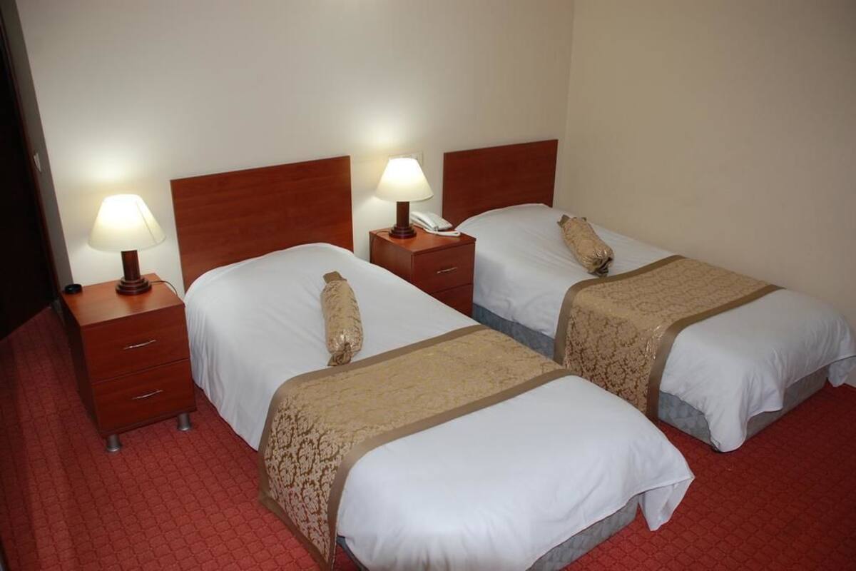 Ein Hotelzimmer mit zwei Einzelbetten, jeweils mit einem Holz-Kopfteil, einem Nachttisch mit Lampe und einem Telefon.