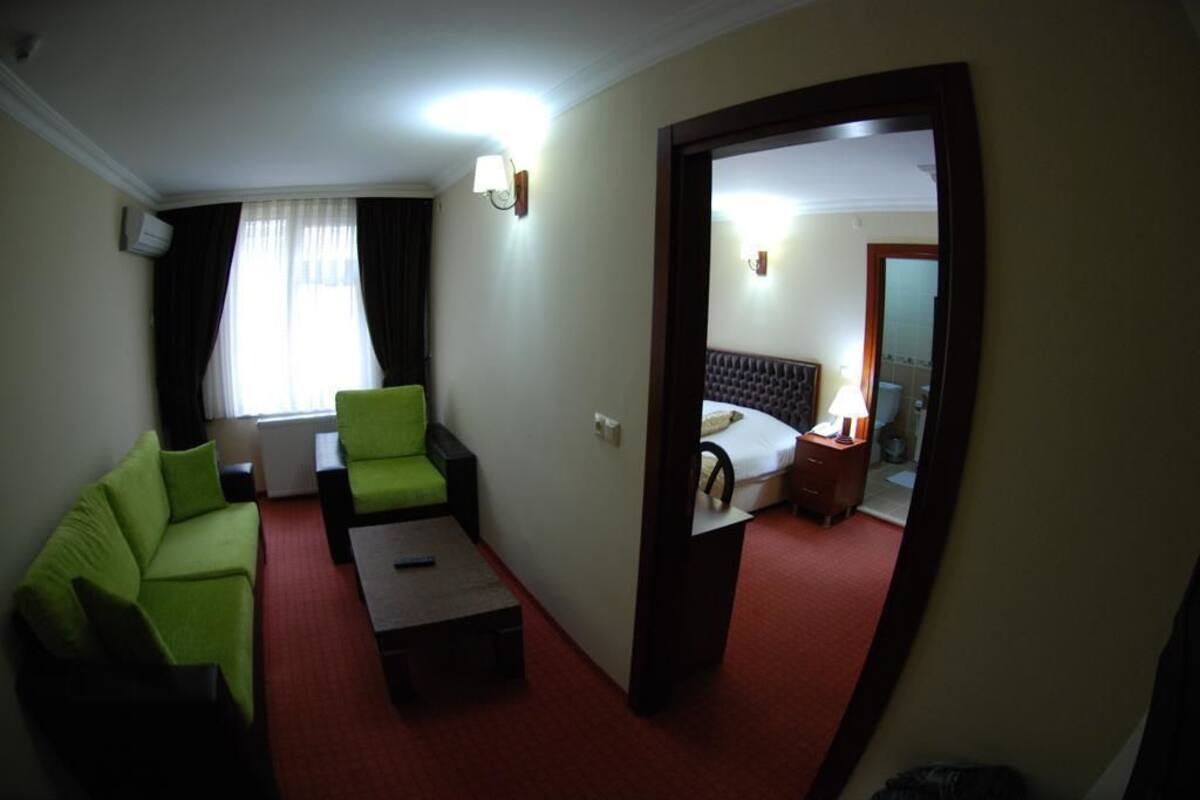 Ein Hotelzimmer mit einem grünen Sofa, einem kleinen Tisch, einem Bett mit Nachttisch und einem Spiegel.