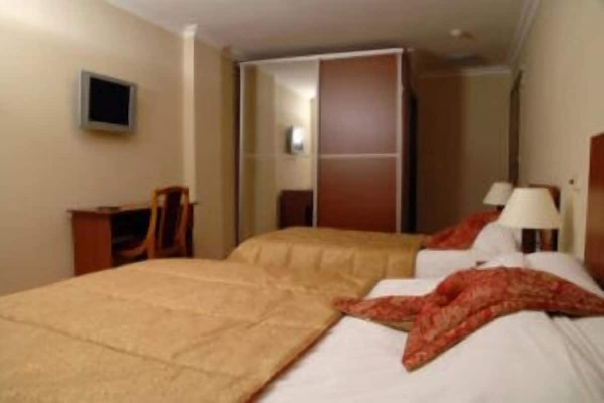 Ein Hotelzimmer mit zwei Betten, einem Schreibtisch, einem Stuhl und einem an der Wand montierten Fernseher.