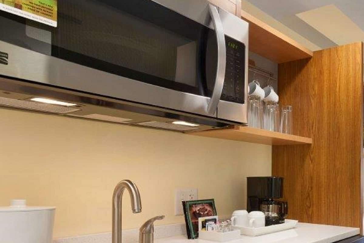 A modern kitchen with a stainless steel microwave, a double sink, and wooden cabinets.