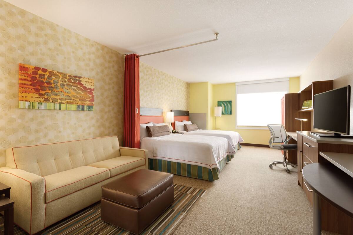 A hotel room with a sofa, two beds, a television, and a desk.