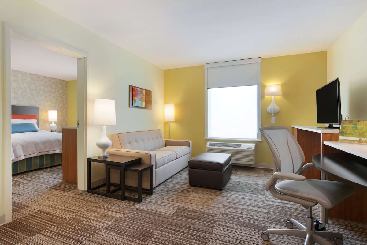 A hotel room with a bed, a sofa, a desk, a chair, and a TV.