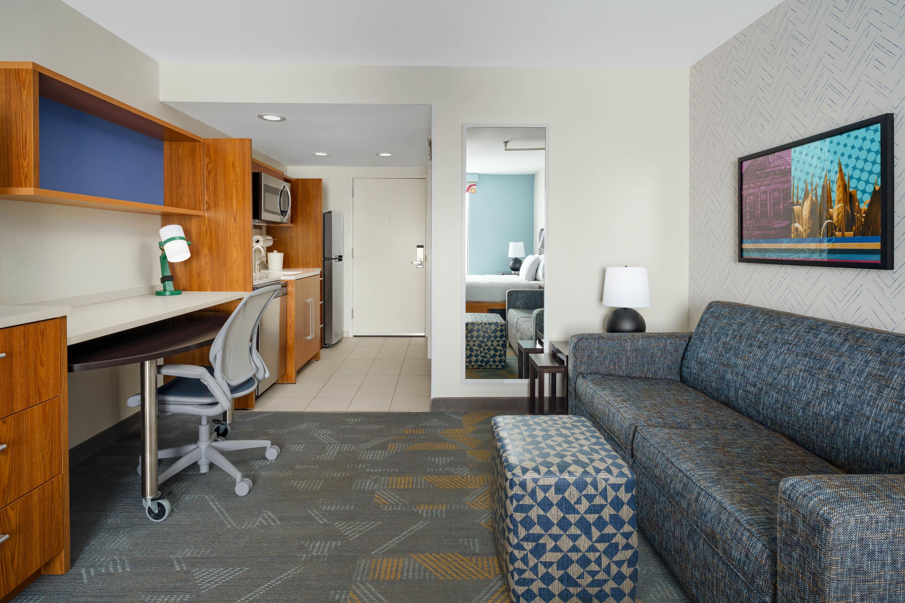 A modern hotel room with a kitchenette, a sofa, a desk with a chair, and a bed.