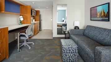 A modern hotel room with a kitchenette, a sofa, a desk with a chair, and a bed.