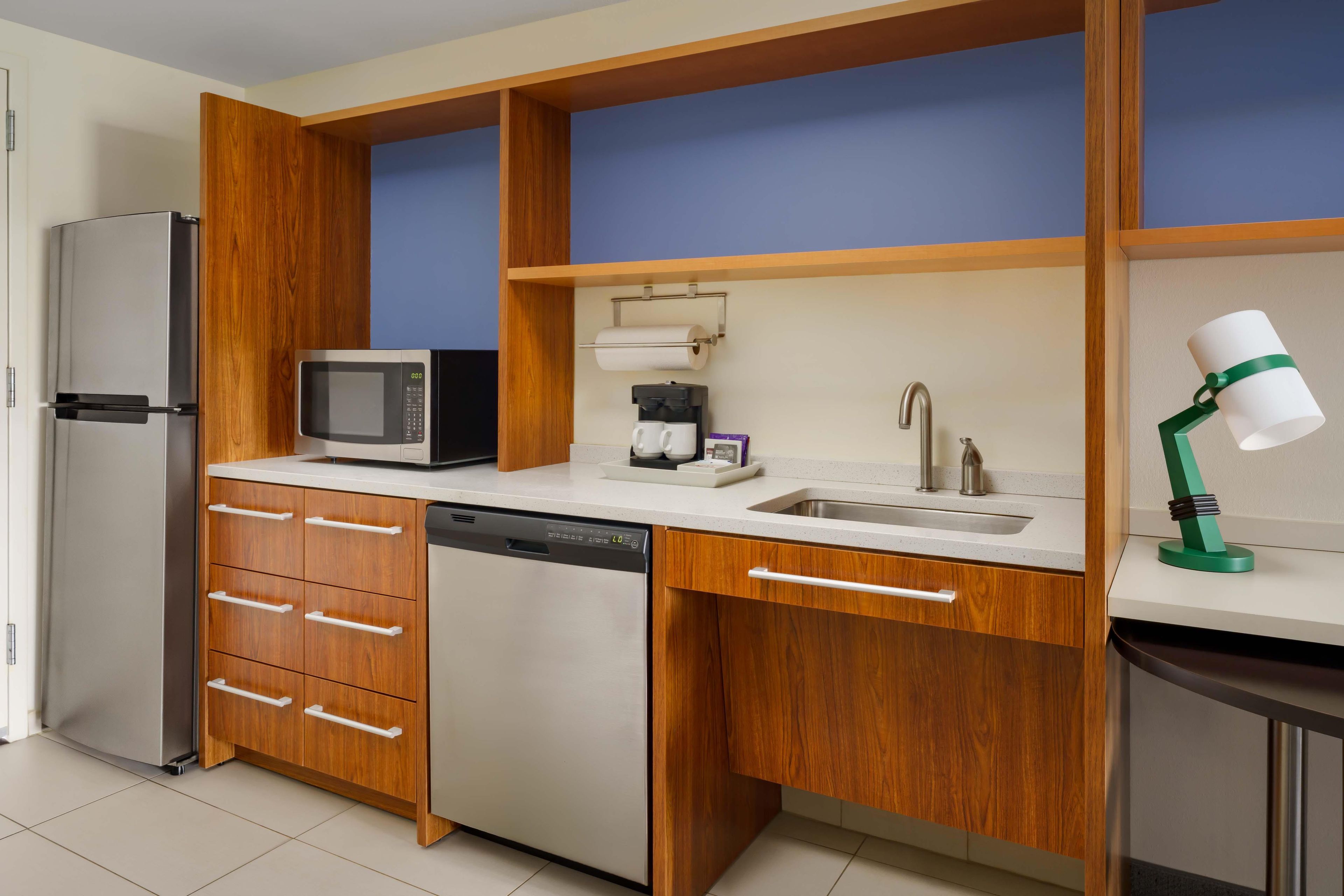A compact kitchen with a refrigerator, microwave, coffee maker, and a sink with a green lamp.