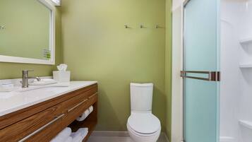 A bathroom with a white toilet, a wooden vanity with a mirror, and a glass shower enclosure.