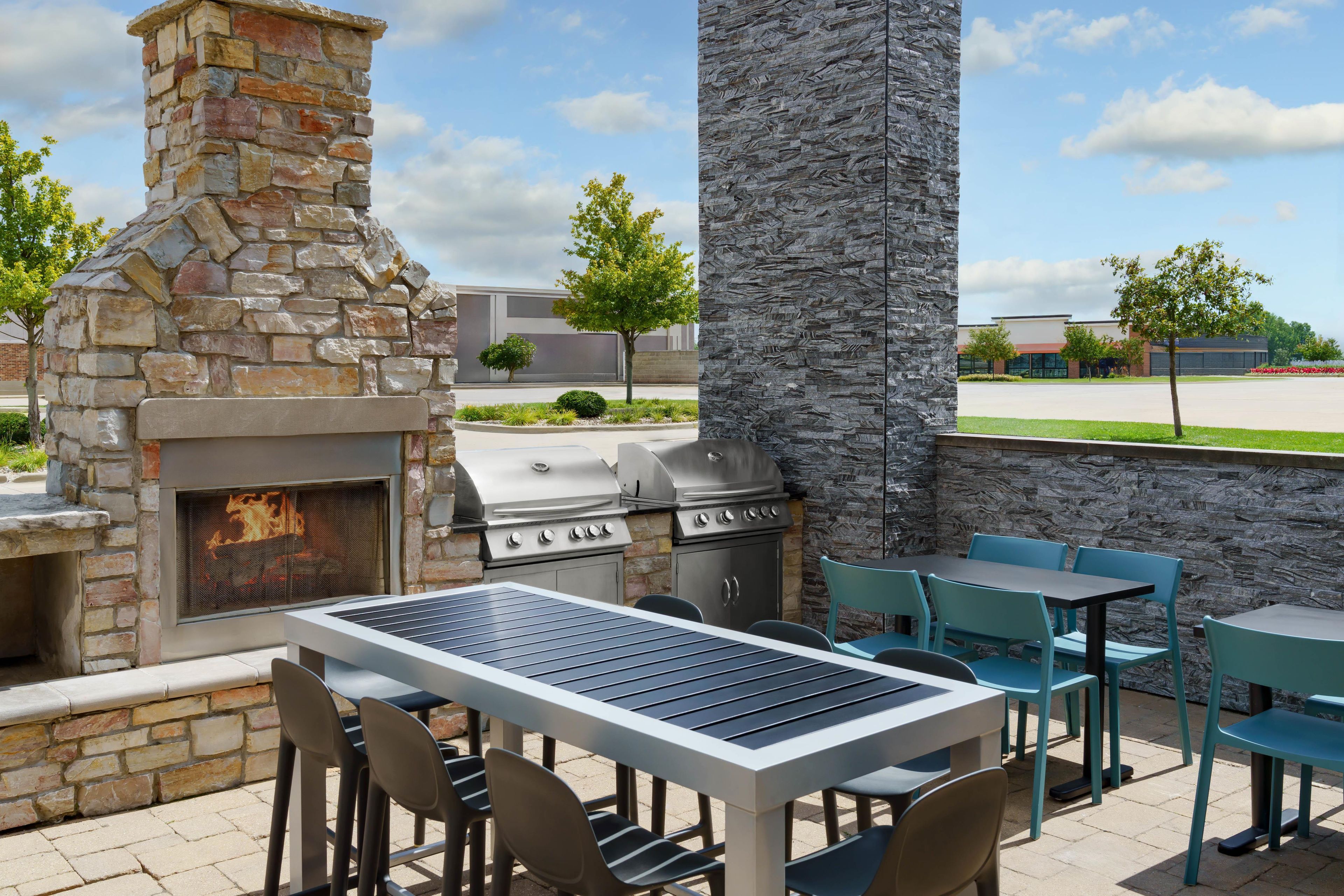 An outdoor patio with a stone fireplace, a grill, and a table with chairs.