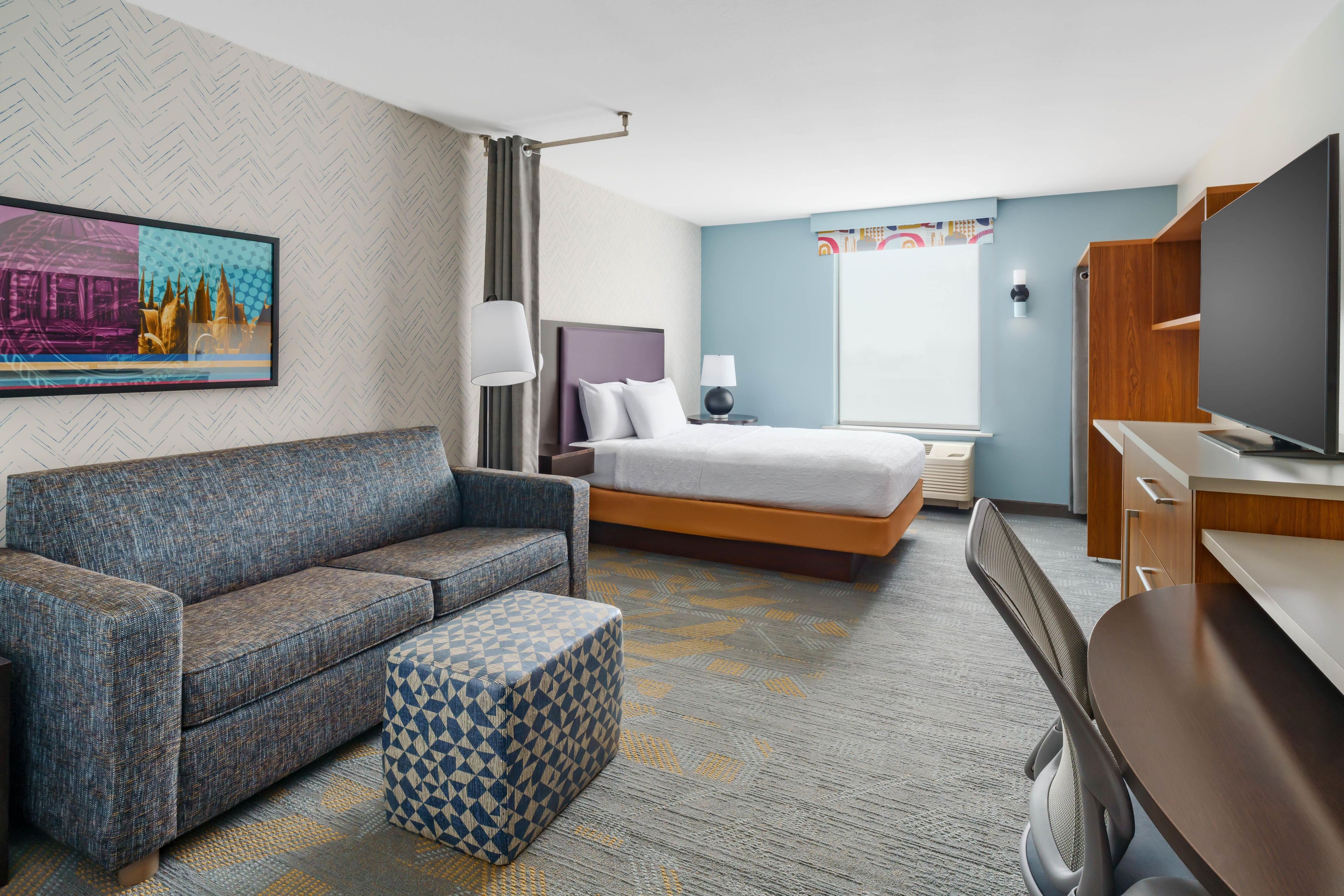 Ein Hotelzimmer mit Sofa, Bett, Fernseher und Schreibtisch.