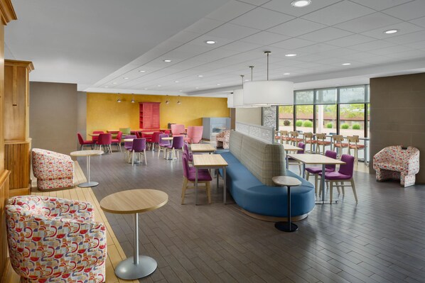 A modern dining area with multiple seating options including tables, chairs, and a sofa. - Home2 Suites by Hilton Champaign/Urbana (Champaign)