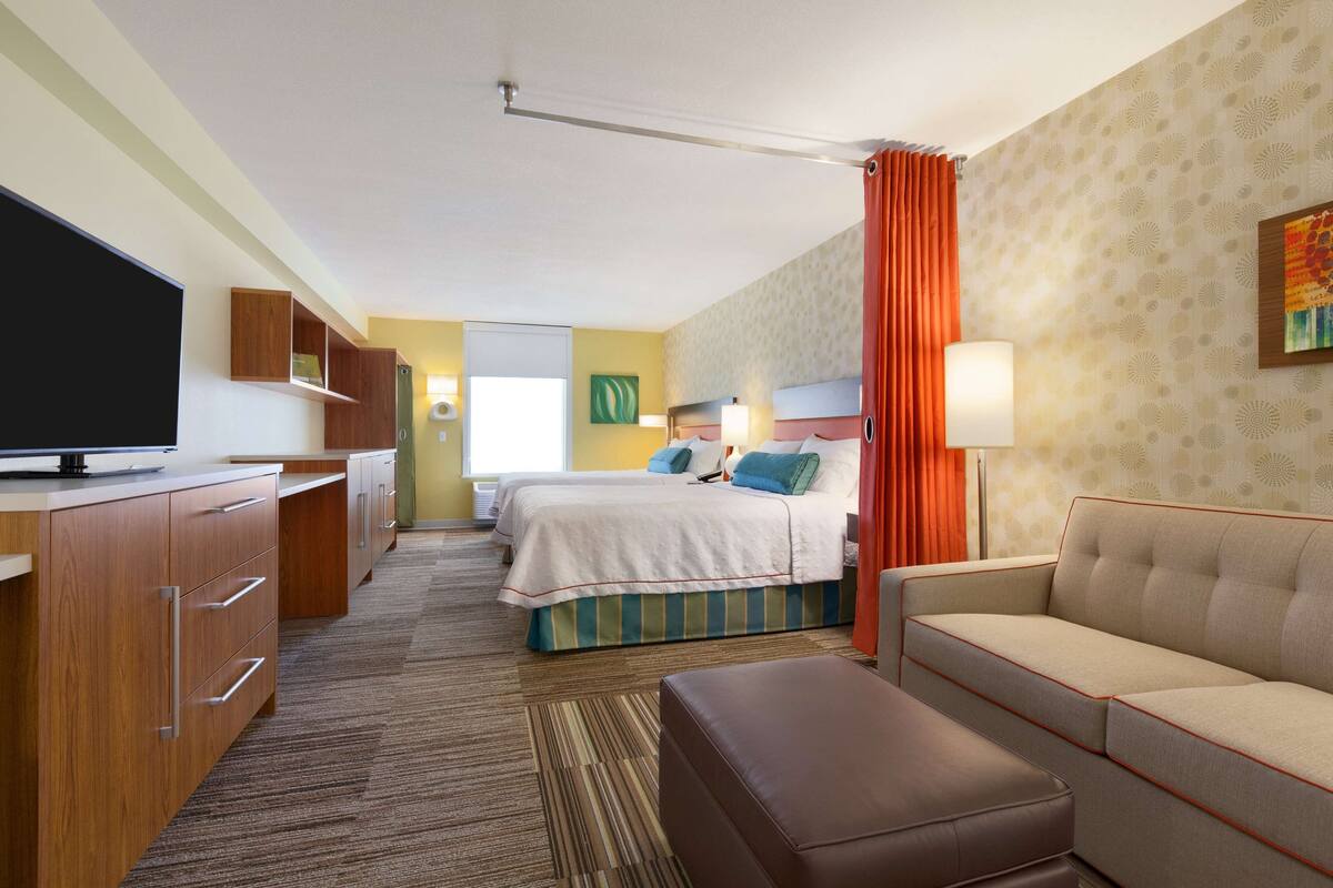 A hotel room with a large flat-screen TV, a sofa, a bed with a striped bedspread, and a desk with drawers.