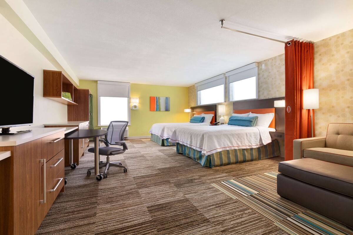 A hotel room with a desk, two beds, a TV, and a sofa.