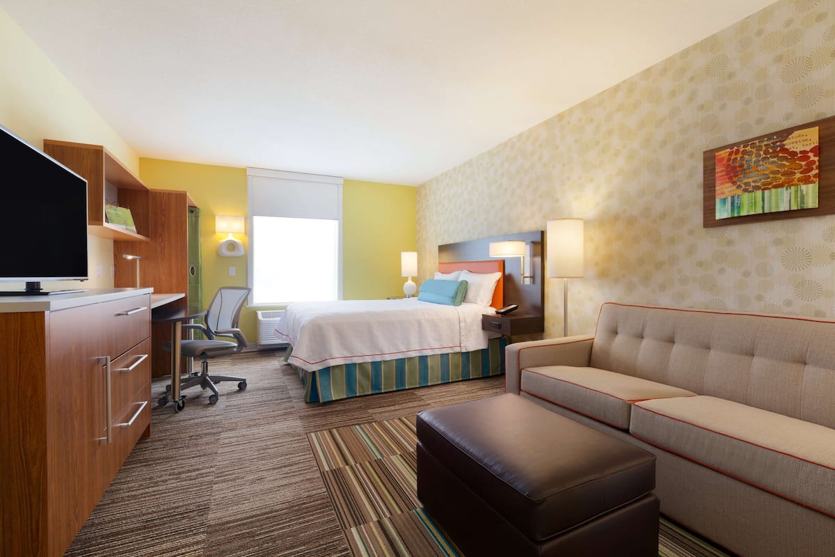 A hotel room with a bed, a sofa, a desk with a computer, a TV, and a lamp.