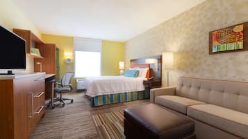 A hotel room with a bed, a sofa, a desk with a computer, a TV, and a lamp.