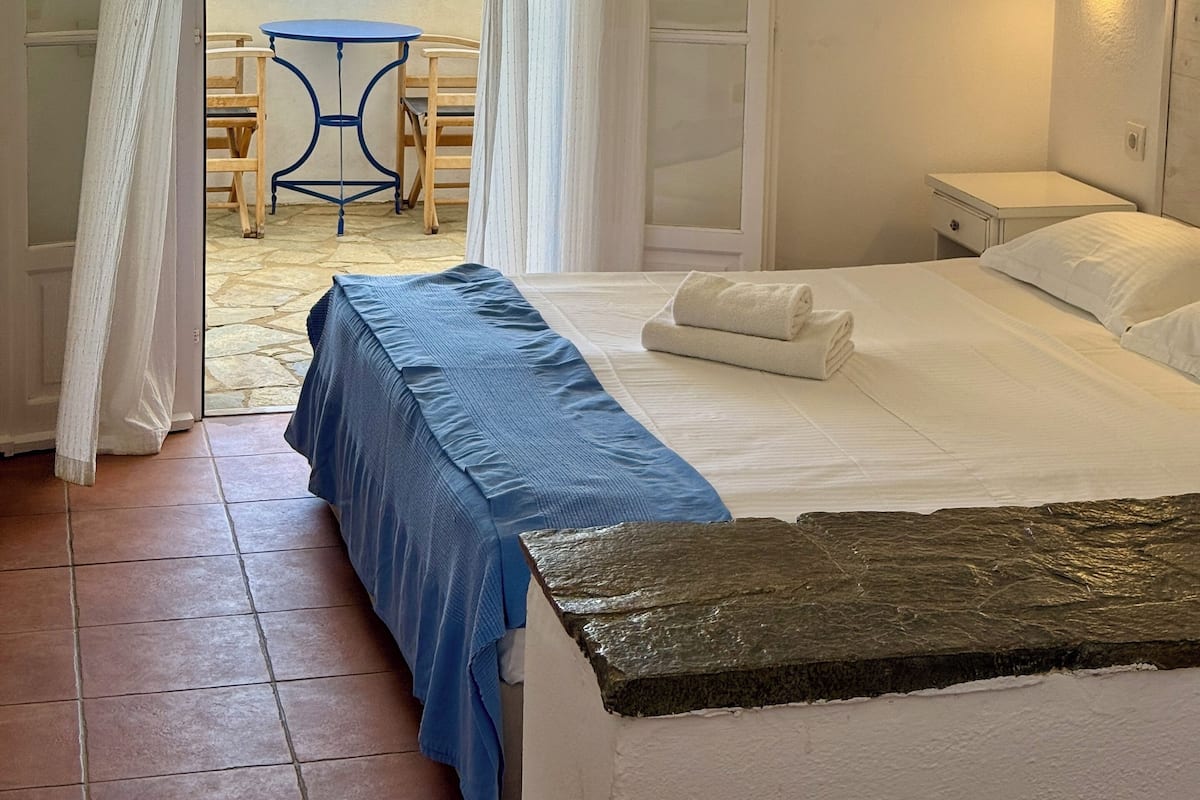 A hotel room with a bed, a small table, and a chair near a window with a view of the sea.