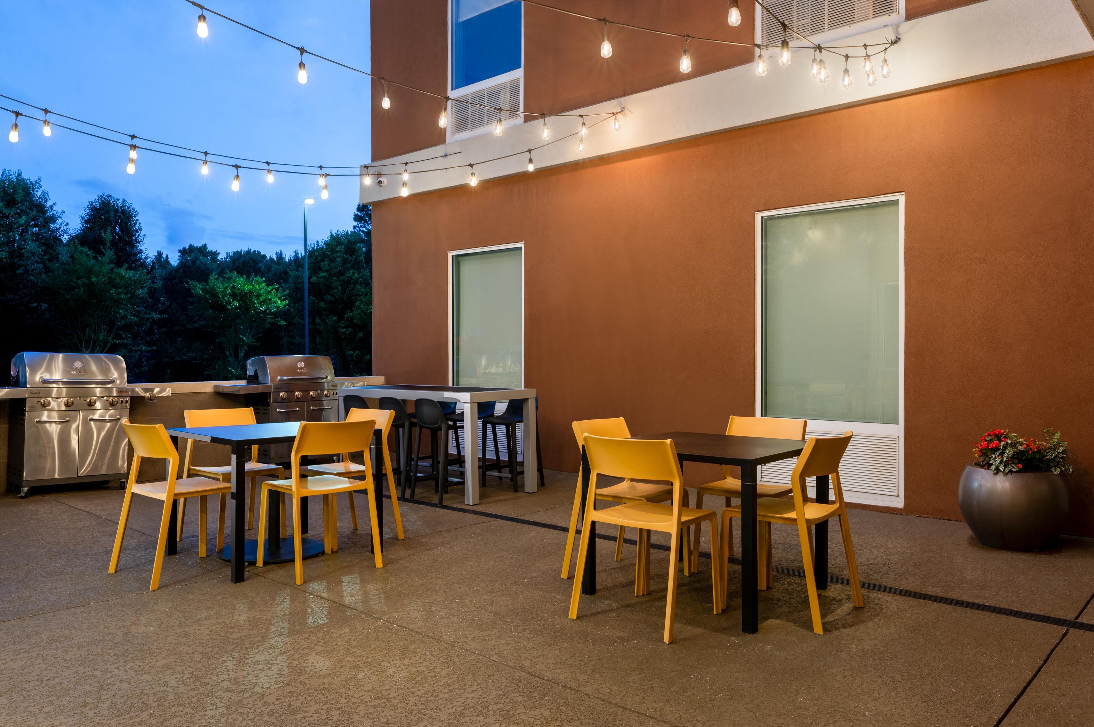 Une terrasse extérieure équipée d’un barbecue, d’une table à manger, de chaises et de guirlandes lumineuses.