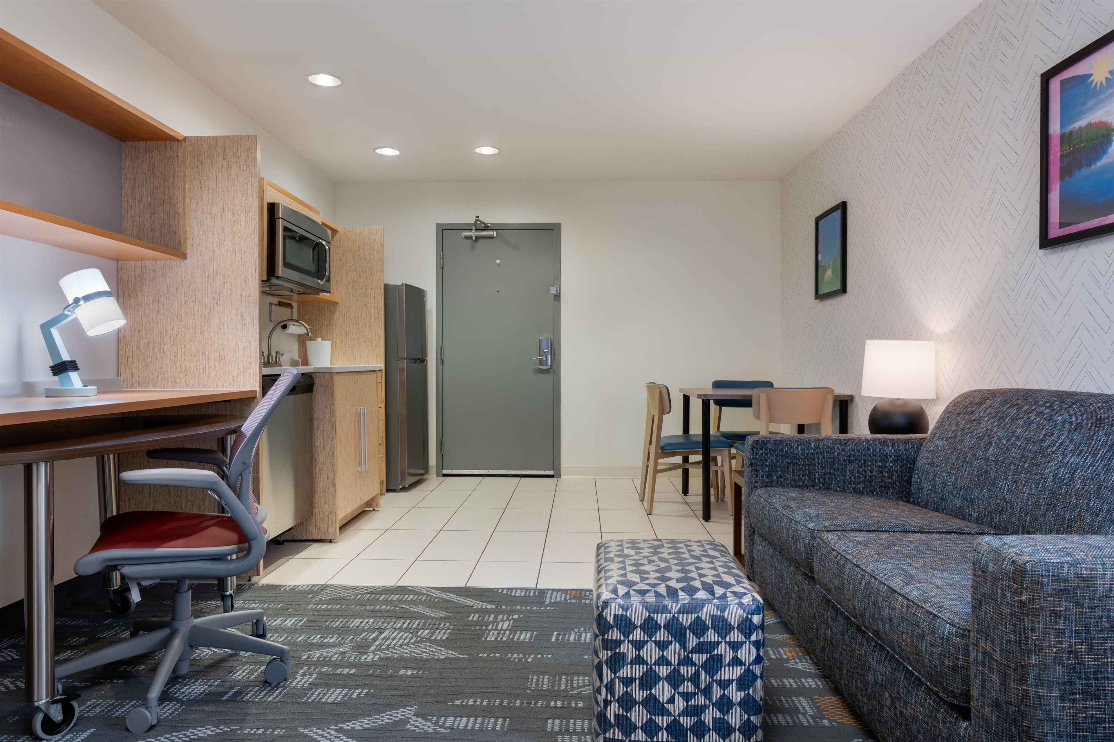Habitación de hotel compacta con kitchenette, sofá, escritorio con silla y zona de comedor.