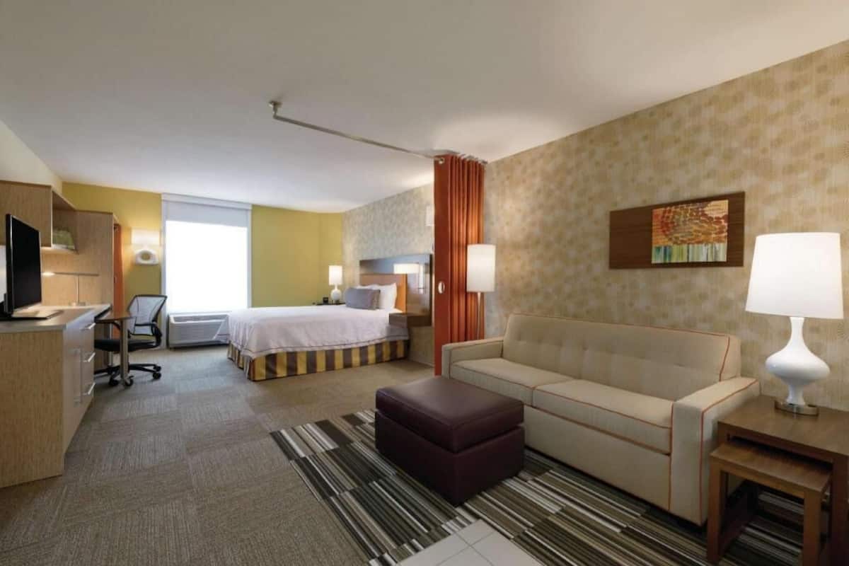 Habitación de hotel con cama, sofá, escritorio con silla, televisión y lámpara.