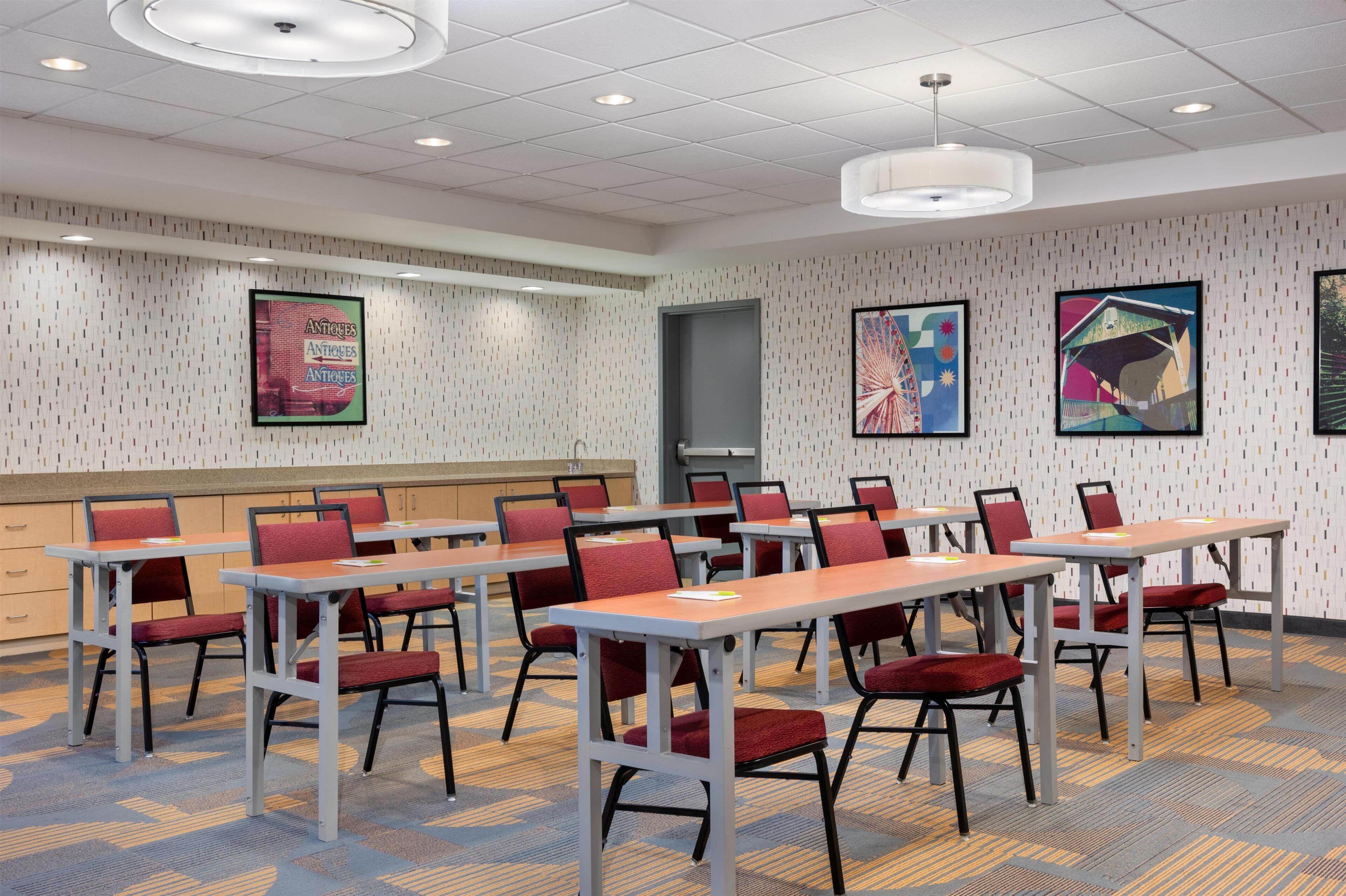 A conference room with tables and chairs, a white patterned wall, and ceiling lights.