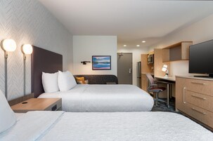 Una habitación de hotel con dos camas, un escritorio, un televisor y un cuadro en la pared.