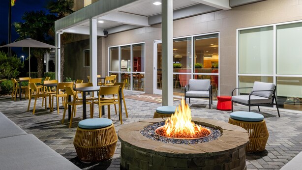 An outdoor patio with tables and chairs, a fire pit, and a building with large windows.