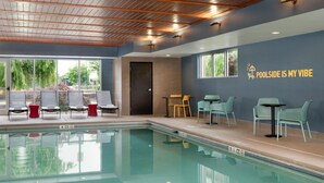 An indoor pool area with lounge chairs, tables, and a poolside sign.