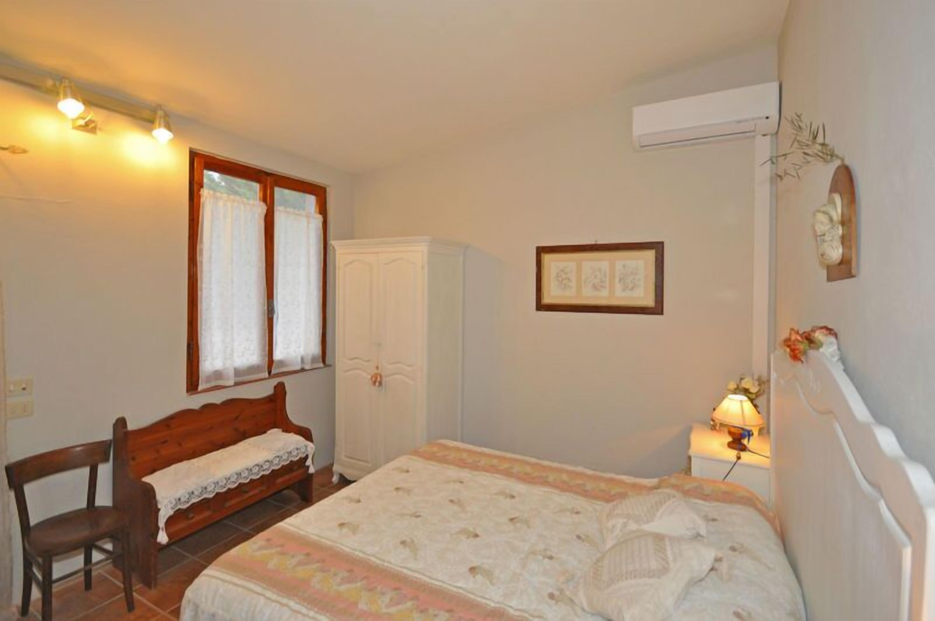 A bedroom with a bed, a wooden bench, a wardrobe, and a nightstand with a lamp.