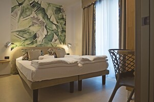Una cama bien hecha con sábanas blancas, un cuadro abstracto grande en la pared y vistas del exterior a través de una ventana con cortinas.